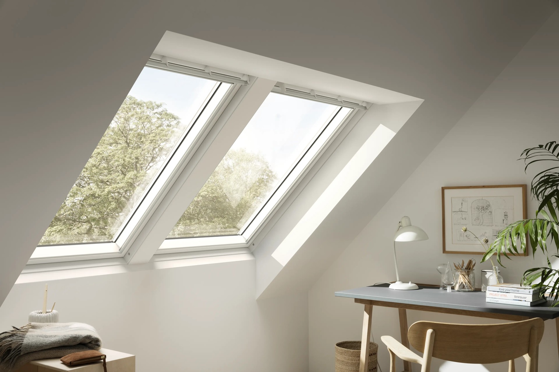 A modern home office featuring a double pitched roof window. The office has simple wooden furniture and house plants